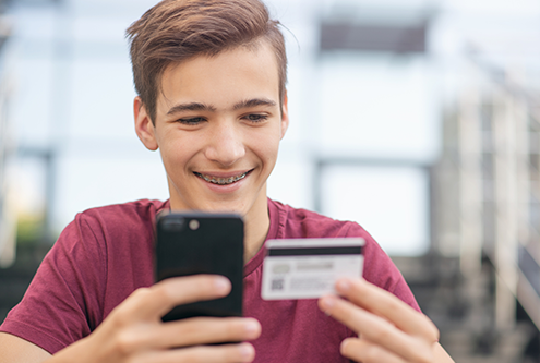 teenage boy using a debit card with his cell phone